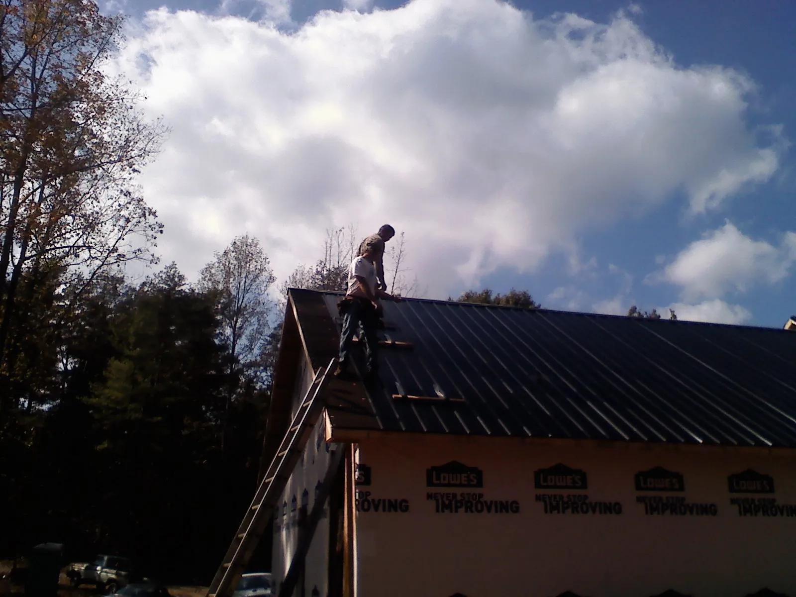 Roofer fastening dark metal panels high against a cloudy sky, from a Roof Inspection job in Ickesburg