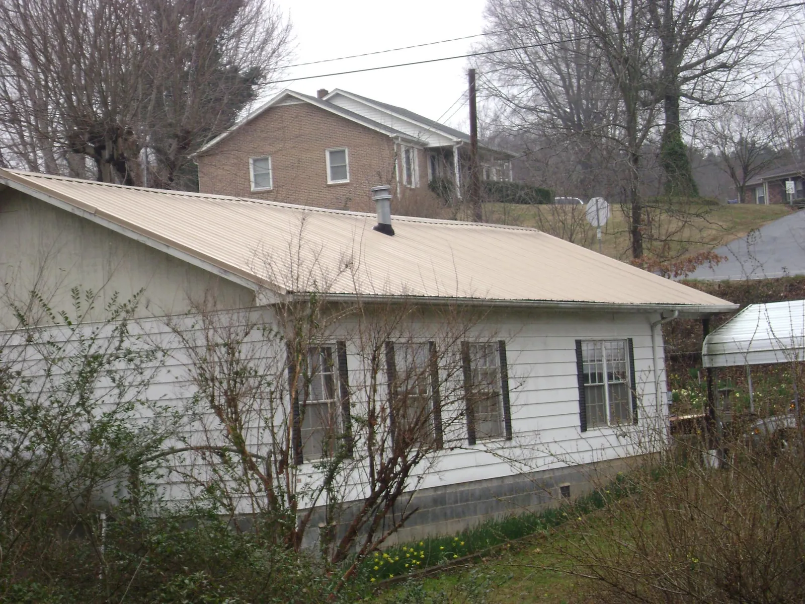 Tan metal roof on a white sided house set into a hillside — Commercial Roofing by Roofing Brothers in Ickesburg